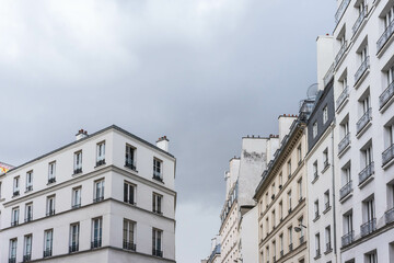 A gray and wintry ambiance envelops Parisian skyscrapers captured from a low-angle view, with a threatening sky hinting at impending rain, casting a soft, bluish light.
