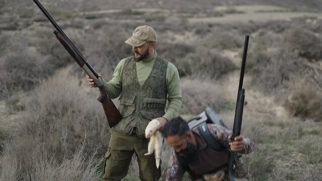 Two Spanish hunters pose with a hunted rabbit and a ferret