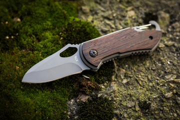 Tactical folding knife with water drops for survival on moss background
