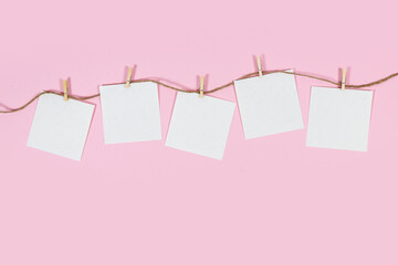 White paper cards on clothes-pegs on pink background