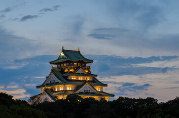 Osaka Castle in Japan at dusk with its interior lights turned on.