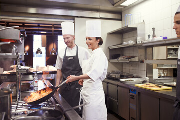 Happy, chefs and cooking with flame in professional kitchen for fine dining, hospitality and...