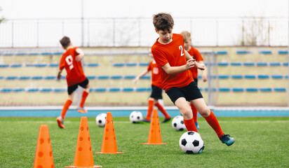 Happy Kids on Training Soccer Drill. Football Summer Camp. Young European Footballers Dribbling Around Cones in Drill. Soccer Boys in Red Uniforms in Training With School Young Coach