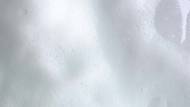 Soap bubbles on window glass. Macro shot of white soap suds flowing down of glass. Shower concept. Cleaning windows, hygiene, disinfection, housework, household, cleanup, washing.