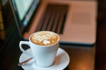 Coffee, art and laptop in cafe on table, warm beverage and internet browsing with tech for online...