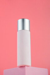 Plastic white tube for cream or lotion. Skin care or sunscreen cosmetic with stylish props on pink background.