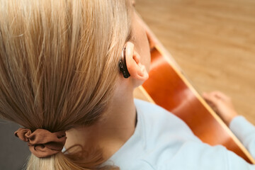 A woman with hearing loss can hear and play guitar again using a hearing aid. Adult woman with hearing aid behind the ear can hear sounds.