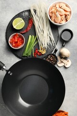 Flat lay composition with black wok, spices and products on grey textured table