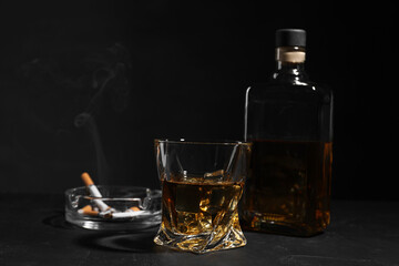 Alcohol addiction. Whiskey, smoldering cigarettes and ashtray on dark textured table