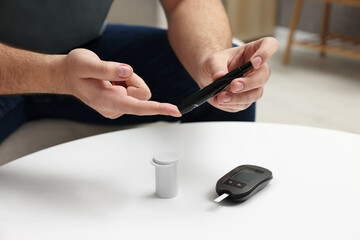 Fototapeta premium Diabetes test. Man checking blood sugar level with lancet pen at white table, closeup