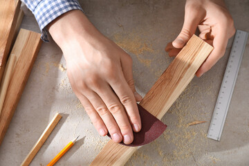 Man polishing wooden plank with sandpaper at grey table, top view