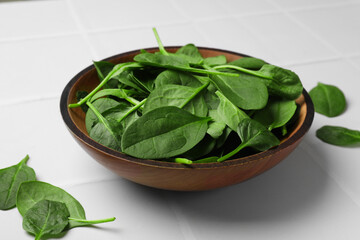 Fresh spinach leaves in bowl on white tiled table, closeup