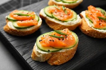 Tasty canapes with salmon, cucumber and cream cheese on grey table, closeup