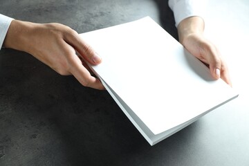 Man holding blank notebook at black textured table, closeup. Mockup for design