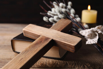 Cross, Bible, burning church candle and willow branches on wooden table, closeup