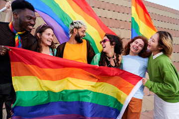 Happy image of a group of LGBTQIA having fun celebrating together at pride day festival outdoors, holding rainbow flags in support of the community and inclusion. Copy space.