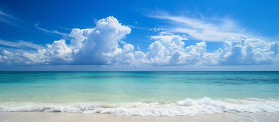 Clear blue sky with fluffy clouds over calm turquoise sea and white sandy beach, with copyspace.