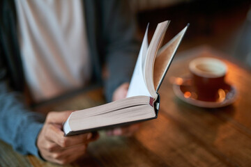 Hands, person and book with coffee at cafe in table for reading novel or story for knowledge....