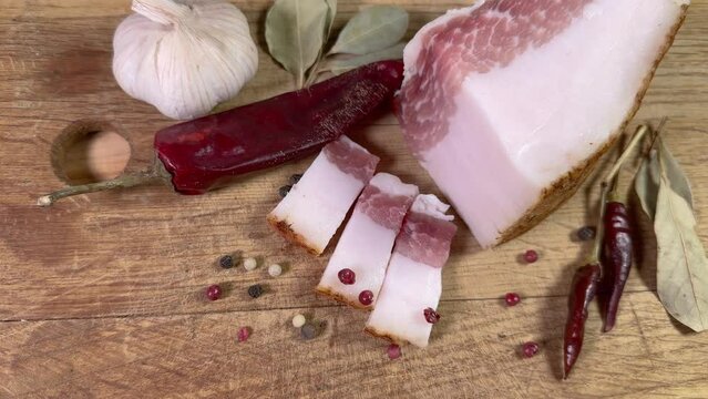 Partly sliced salted pork fatback among spices on cutting board