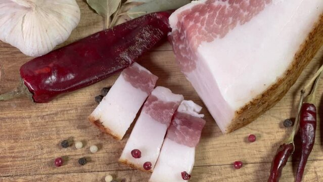 Partly sliced salted pork fatback among spices on cutting board