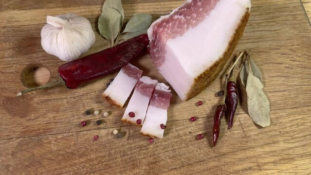 Partly sliced salted pork fatback among spices on cutting board