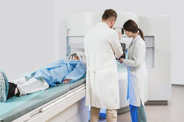 two doctors and a patient in the MRI room. Male doctor and female assistant preparing adult female...