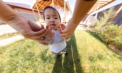 Close-up of a parent hands and a cute little Asian girl. Sweet Korean baby outdoors on a lawn with...