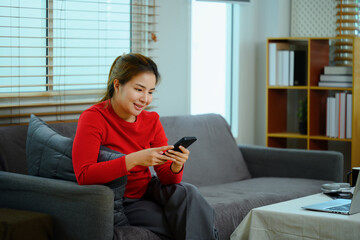 Pleased young Asian woman texting messages, chatting in social on her smartphone - obrazy, fototapety, plakaty