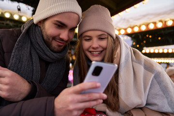 Young couple browsing phone together on Christmas Market at night