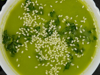 Fresh green pea puree soup with white sesame seeds  in a white bowl, background 