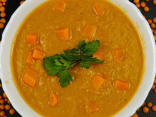 Red lentil puree soup with pumpkin pieces in a white bowl and fresh green parsley, background 