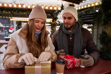 Caucasian couple opening presents on Christmas market - obrazy, fototapety, plakaty