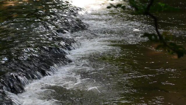 Sun rays falling on a waterfall on a river in a valley with ferns.