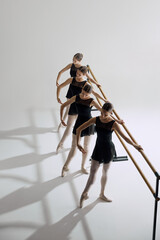 Four elegant girls, ballet dancers standing at barre and warming up, practicing against grey studio...