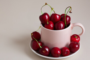 cherries in a mug. on a white table there is a large light mug with large ripe red cherries, fruit concept