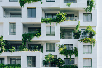 Fototapeta na wymiar Facade of a white modern apartment building with balconies covered in lush green plants
