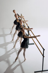 Four teens girls, ballet dancers practicing at barre, extending arm in delicate gesture against grey studio background. Concept of ballet, art, dance studio, classical style, youth - obrazy, fototapety, plakaty