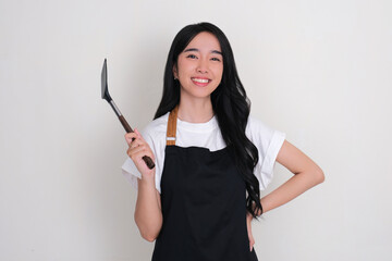 An Asian woman wearing apron showing happy face expression while holding spatula