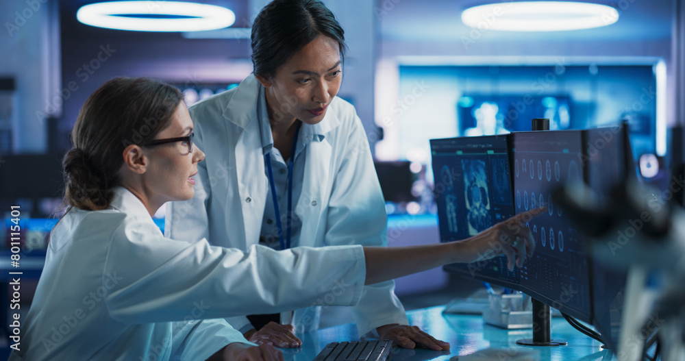 Poster Asian And Caucasian Female Doctors Talking In Medical Research Center And Using Desktop Computer To Analyze MRI Scans Of Brain. Surgeon And Neuroscientist Discussing Solutions For Treating Cancer.
