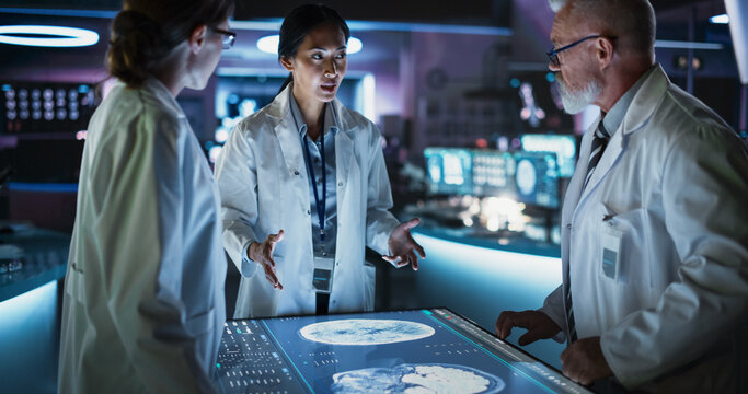 Modern Hospital Medical Research Center: Diverse Colleagues Gathered Around Interactive Touch Screen Table With MRI Scans Of Brain On Display. Doctors Discussing Rehabilitation Solutions After Stroke.