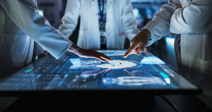 Hospital Medical Research Center: Focus On Hand Gestures Of Diverse Colleagues Gathered Around Interactive Touch Screen Table With MRI Scans Of Brain On Display. Doctors Looking For Alzheimer's Cure.