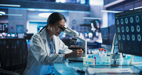 Medicine Development Laboratory: Asian Female Scientist Using Microscope, Analyzes Petri Dish Sample. Big Pharmaceutical Lab with Specialists Conducting Biotechnology Research, Developing New Drugs.