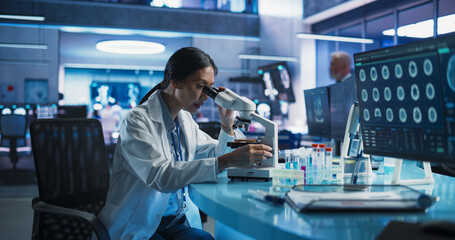 Medicine Development Laboratory: Asian Female Scientist Using Microscope, Analyzes Petri Dish...