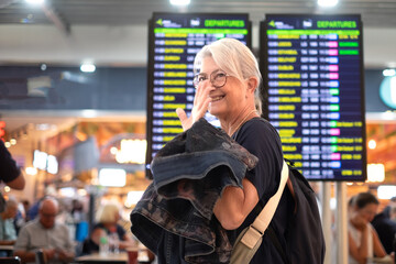 Woman traveler - senior lady standing inside airport terminal looking at timetable schedule. Travel...