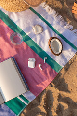 Wireless headphones, notepad, glass of water and coconut on the striped towel on the sand. Summer vacation lifestyle concept