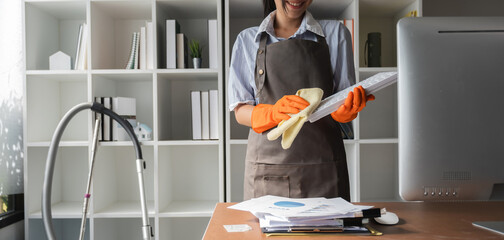 Young Asian housewife cleans the work desk in the office using a dust cloth.