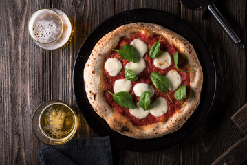Pizza Margherita with basil and two glasses of beer on a black plate. View from above