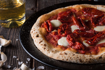 A slice of pizza with mozzarella and sun-dried tomatoes on a black plate and a glass of beer. Side...