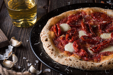 A slice of pizza with mozzarella and sun-dried tomatoes on a black plate and a glass of beer. Side view, close up.
