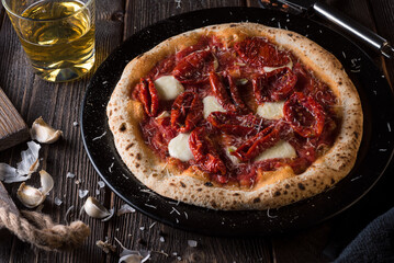 Pizza with mozzarella and sun-dried tomatoes on a black plate and a glass of beer. Side view.